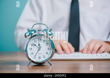 Concept de temps de travail pour les professionnels, homme d'affaires travaillant et tapant sur un ordinateur portable avec horloge sur le bureau. Banque D'Images