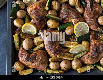 Des cuisses de poulet cuites avec des pommes de terre et des courgettes sur une plaque de cuisson Banque D'Images