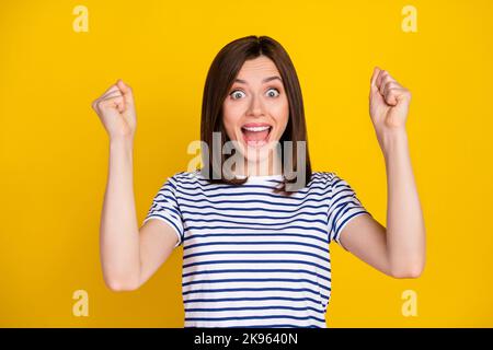 Portrait de positive gaie mignonne fille avec la coiffure droite vêtements rayés t-shirt shout ouais Fists up isolé sur fond jaune de couleur Banque D'Images