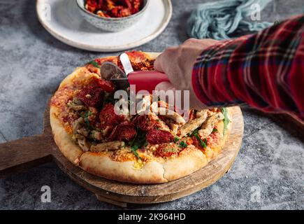 La main de l'homme tient le couteau sur une pizza italienne chaude sur fond de marbre gris. Banque D'Images