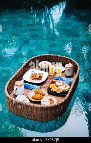 Le plateau de petit-déjeuner en rotin synthétique flotte sur la piscine tropicale d'Ubud, Bali Banque D'Images