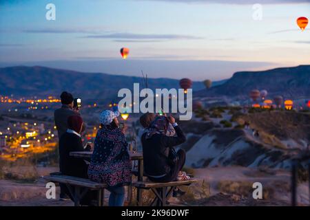 Les touristes assis sur le banc au sommet de la colline en prenant des photos de ballons d'air chaud volant au-dessus de la Cappadoce la nuit. Ciel coloré. Prise de vue horizontale en extérieur. Photo de haute qualité Banque D'Images