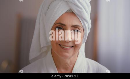 Gros plan sourire heureux attrayant senior caucasien mature grand-mère 60s femme d'âge moyen portant un peignoir et une serviette blanche sourire regardant l'appareil photo avec Banque D'Images