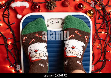 Une femme en chaussettes de Noël se tient sur la balance, se pèse après la gourmandise pendant les vacances Banque D'Images