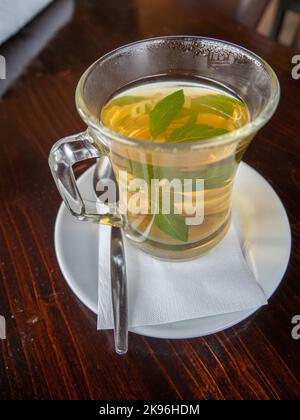Gros plan vertical de thé aromatique sain à la menthe fraîche dans une tasse en verre transparent sur une table en bois sombre Banque D'Images