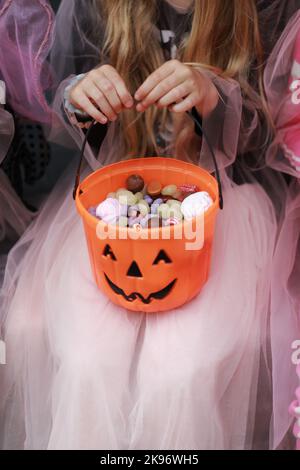 Photo courte d'une fille dans une robe sorcière fantaisie tenant un panier de bonbons en forme de citrouille avec visage effrayant dans ses mains. Trick ou traiter. Doux différent Banque D'Images