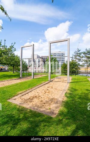 Overheight rustiques balançoires dans un terrain de jeu à Baakenpark à Hambourg, Hafencité. Une surface de sable bordée de poutres en bois sert de protection contre les chutes. Le Banque D'Images