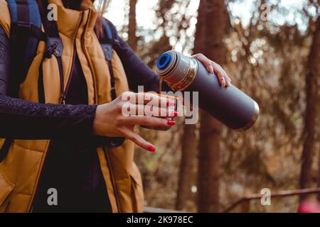 Femme Backpacker tient thermos avec une boisson chaude à la main à l'automne forêt, nature. Concept de voyage et de camping. Boisson réchauffante Banque D'Images