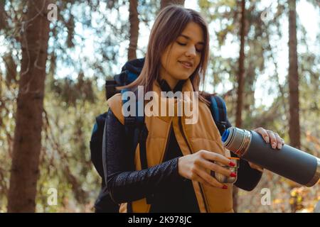 Femme Backpacker tient thermos avec une boisson chaude à la main à l'automne forêt, nature. Concept de voyage et de camping Banque D'Images