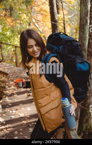 Femme Backpacker tient thermos avec une boisson chaude à la main à l'automne forêt, nature. Concept de voyage et de camping. Boisson réchauffante Banque D'Images