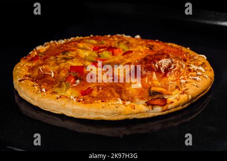 Pizza maison brûlée sur plateau dans four électrique, fond noir Banque D'Images