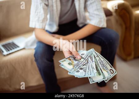 Billets de banque en papier entre les mains d'un enfant. Un fan de billets de cent dollars dans les mains d'un adolescent. Vous avez gagné de l'argent en ligne pour vos achats le Vendredi fou. Banque D'Images