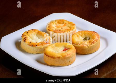 Mini quiches en-cas de saveurs variées sur une assiette blanche. Banque D'Images