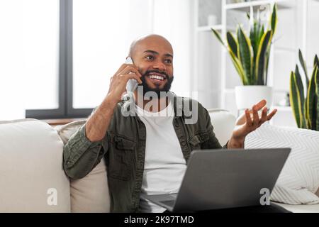 Homme d'affaires latin positif parlant au téléphone portable tout en étant assis sur un canapé avec ordinateur portable, espace de copie Banque D'Images