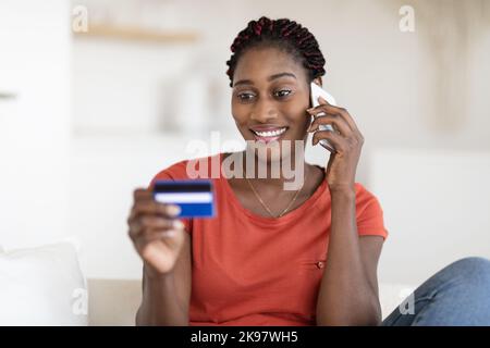 E-commerce. Souriant Afro-américain Femme tenant une carte de crédit et parlant au téléphone portable Banque D'Images
