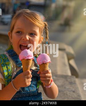 Jolie petite fille avec deux crèmes glacées à l'extérieur. Banque D'Images