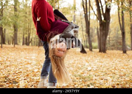 Une femme tient dans les mains gaie école fille âgée couchée tête vers le bas. Bonne mère et fille dans les sweaters tricotés confortables ont le plaisir et de marcher en automne doré Banque D'Images