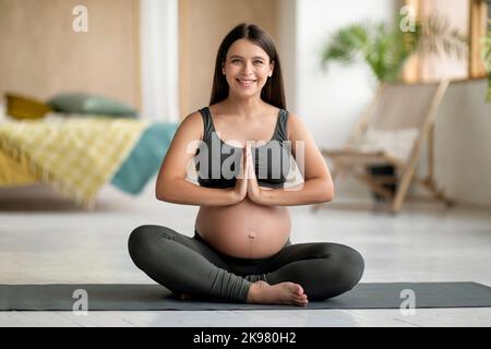 Portrait d'une jeune femme enceinte heureuse pratiquant le yoga à la maison Banque D'Images