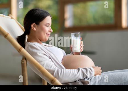 Jeune femme souriante plaçant du verre avec du lait sur son ventre enceinte Banque D'Images
