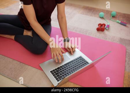 Jeune femme assise sur le tapis de yoga et à la recherche de vidéo de la forme physique préférée blogger Banque D'Images