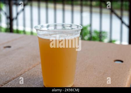 Un grand verre en plastique transparent de bière artisanale aigre dans une microbrasserie. Le verre en plastique contient du givre sur le rafraîchissement froid. La bière est sur une table en acrylique. Banque D'Images