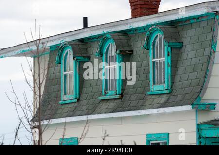 Un bâtiment en bois blanc de style vintage avec garniture bleu sarcelle, des fenêtres à une caisse, des dortoirs en forme de arche et un toit en mansarde noir. La maison Banque D'Images