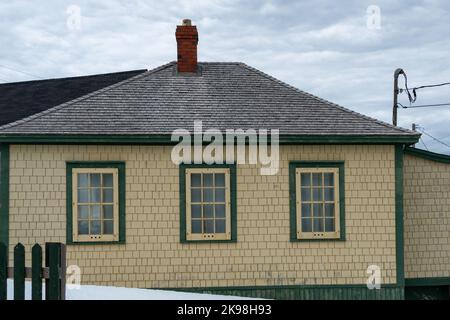 Une maison en panneaux de bois de cèdre jaune d'époque avec un toit en bois gris à la hanche. Le bâtiment a une cheminée en briques rouges et de multiples fenêtres en verre. Banque D'Images