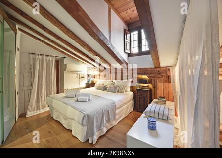 Chambre d'une ancienne maison située dans le grenier avec des plafonds mansardés avec parquet en chêne et poutres apparentes Banque D'Images