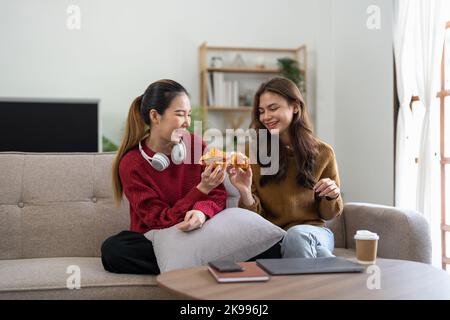 Deux amis qui apprécient de manger un croissant assis sur un canapé dans le salon à la maison Banque D'Images