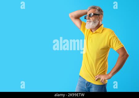 Homme barbu senior dans des lunettes de soleil sur fond bleu Banque D'Images