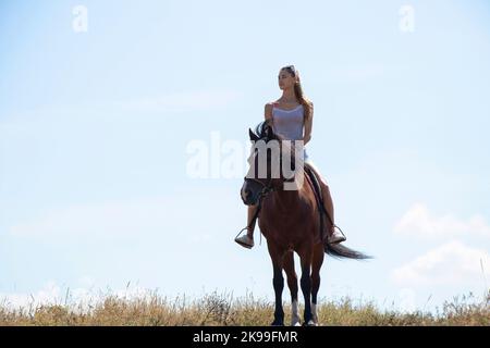 une fille assise à cheval contre le ciel par une journée ensoleillée Banque D'Images