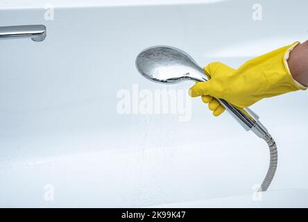 Personne utilisant la pomme de douche à main. Main gantée tenant la pomme de douche. Main tient la pomme de douche avec l'eau couler, espace de copie Banque D'Images