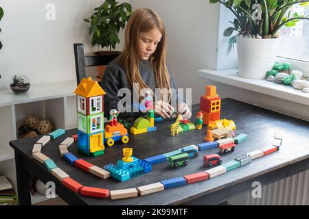 Le garçon de 8 ans joue des cubes et des blocs . Il a construit une ville et un chemin de fer. Activités de loisirs et loisirs à la maison. Un petit inventeur. Photo horizontale. Banque D'Images