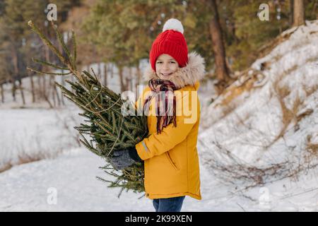 Joyeux enfant tenant dans les mains couper l'arbre de noël sur le fond de forêt enneigée. Garçon avec sapin de Noël. Concept de vacances d'hiver, traditions et ce Banque D'Images