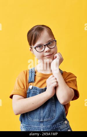 Portrait d'une jeune fille atteinte d'un syndrome de Down regardant l'appareil photo et portant des lunettes sur fond jaune en studio Banque D'Images