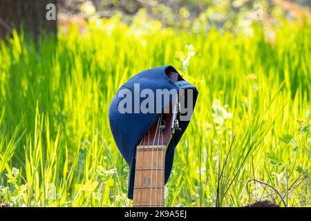 casquette de baseball bleue suspendue sur une vieille guitare se tient sur un fond d'herbe Banque D'Images