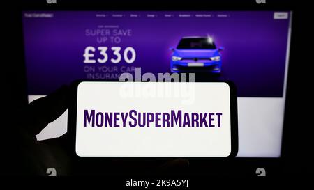 Personne tenant un smartphone avec le logo de la société britannique Moneysupermarket.com Group PLC à l'écran devant le site. Mise au point sur l'affichage du téléphone. Banque D'Images