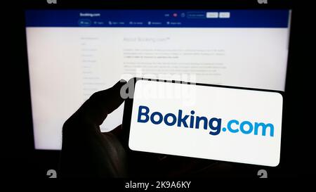 Personne tenant un smartphone avec le logo de l'agence de voyage en ligne néerlandaise Booking.com sur l'écran devant le site Web. Mise au point sur l'affichage du téléphone. Banque D'Images