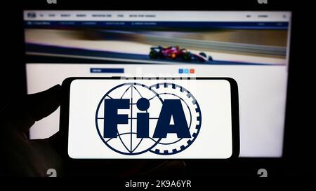 Personne tenant un téléphone portable avec le logo de la Fédération internationale de l'automobile (FIA) à l'écran en face de la page web. Mise au point sur l'affichage du téléphone. Banque D'Images
