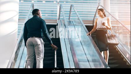 Même objectif, chemins différents. Deux jeunes hommes d'affaires saluent tout en se transmettant sur les escaliers roulants dans un lieu de travail moderne. Banque D'Images