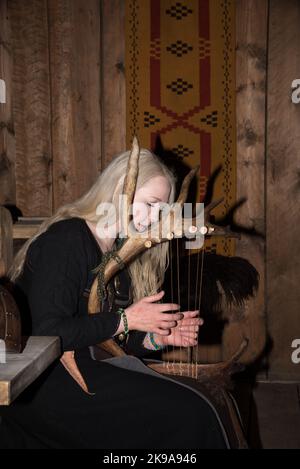 Une actrice viking jouant un instrument à cordes semblable à une harpe dans la maison de la chefferie Viking à Borg sur l'île Vestvågøya, dans l'archipel Lofoten, en Norvège. Banque D'Images