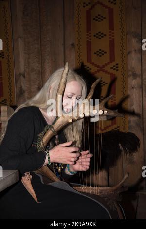 Une actrice viking jouant un instrument à cordes semblable à une harpe dans la maison de la chefferie Viking à Borg sur l'île Vestvågøya, dans l'archipel Lofoten, en Norvège. Banque D'Images