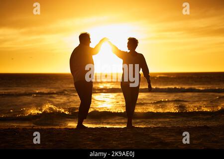 Amour, océan et coucher de soleil, silhouette de couple sur la plage tenant les mains à Bali. Vagues, romance et homme et femme dansant le soir au soleil sur romantique Banque D'Images