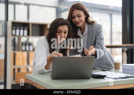 Deux professionnels multiethniques intelligents travaillent ensemble avec un ordinateur portable tout en parlant de nouvelles d'emploi au bureau. Banque D'Images