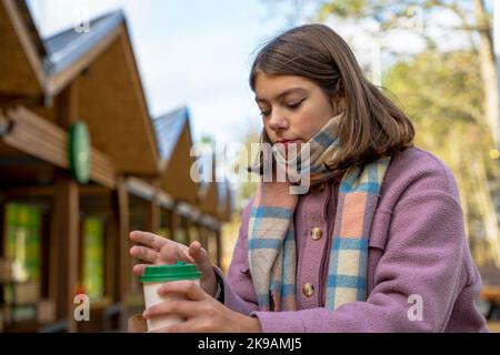 une fille en manteau mange de la nourriture de rue debout à une table dans un café extérieur Banque D'Images