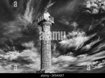 Un phare s'élève contre un ciel rempli de nuages plus sombres. Une ailette d'étanchéité est montée sur le dôme en haut. Banque D'Images