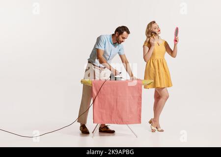 Portrait de l'homme qui fait le repassage tandis que la belle femme qui fait son maquillage isolé sur fond blanc. Porte-maison Banque D'Images