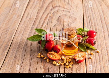 une bouteille de verre avec un liège avec de l'huile de rosehip naturelle sur la table du village parmi les hanches fraîchement cueillies de rose. produit biologique Banque D'Images