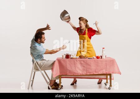 Portrait d'un jeune couple émotif fort, en train de se quereller agressivement tout en prenant le petit déjeuner isolé sur fond blanc. Banque D'Images