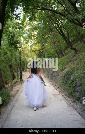 Mariée marchant sur un chemin de forêt seule avec des chaussures dans ses mains Banque D'Images